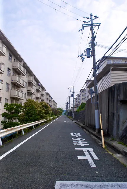 団地とガードレールに沿って下る、「止まれ」の文字のある坂道