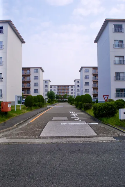 白い団地の建物が両側に並ぶ、まっすぐな団地の中の道