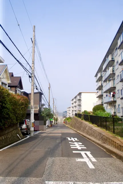 電柱の並ぶ住宅街から、団地の方へまっすぐ下る坂道
