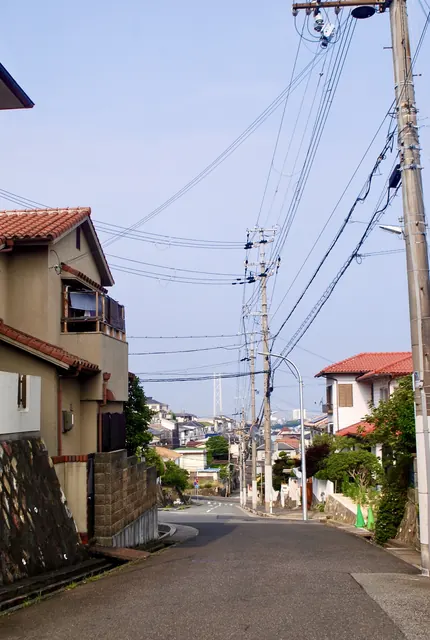 カーブする坂道と家々の向こうに、明石海峡大橋の主塔が見える風景