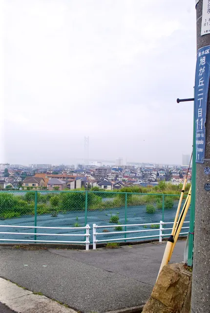 町名表示の電柱の先に、家並みと明石海峡大橋が見える丘の上