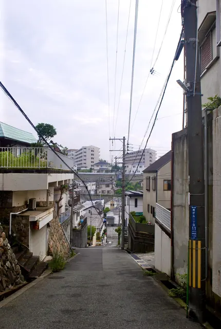 町名表示のある電柱の脇から、家々のあいだを下る坂道