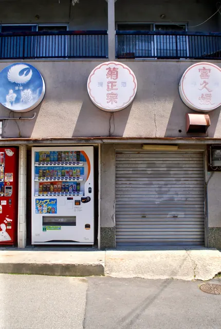 清酒の丸い看板が並び、自動販売機とシャッターのある店先