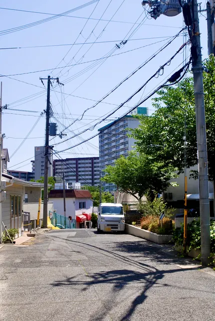 電線の張られた坂道の先に、住宅と大きな団地が見える風景