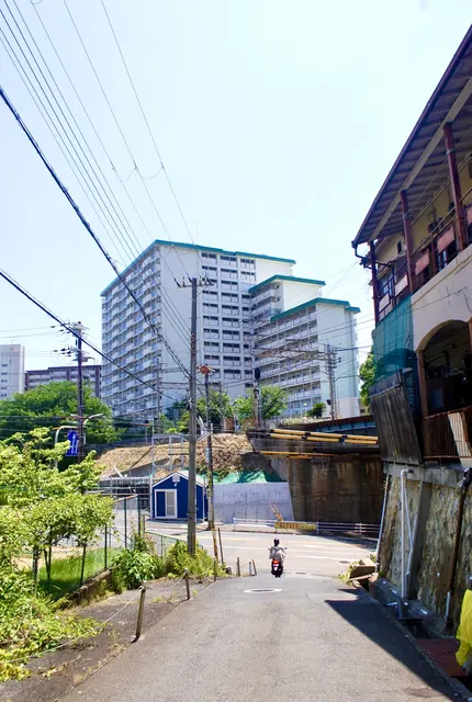 線路の土手の脇の道から、大きな団地を見上げる風景