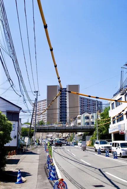 電線が空を横切る大通りの先に、高架と大きな団地が見える風景