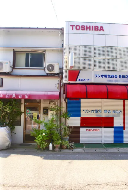 赤いテントの電気店と、ピンクの日よけの美容室が並ぶ店先