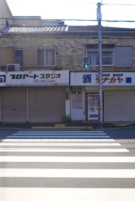 横断歩道の向こうに、シャッターの下りた写真店と酒店が並ぶ風景