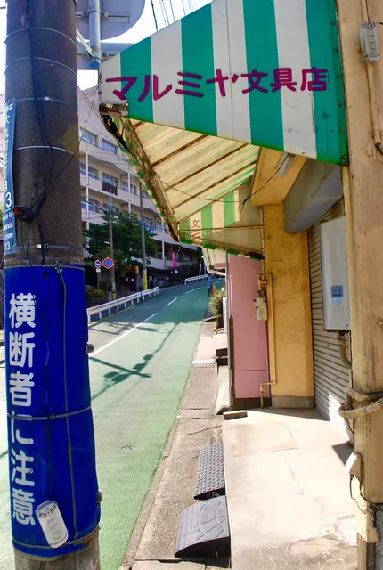 緑と白の縞模様の日よけの文具店と、自転車レーンの通り