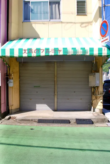 緑と白の縞の日よけの下で、シャッターの下りた文具店