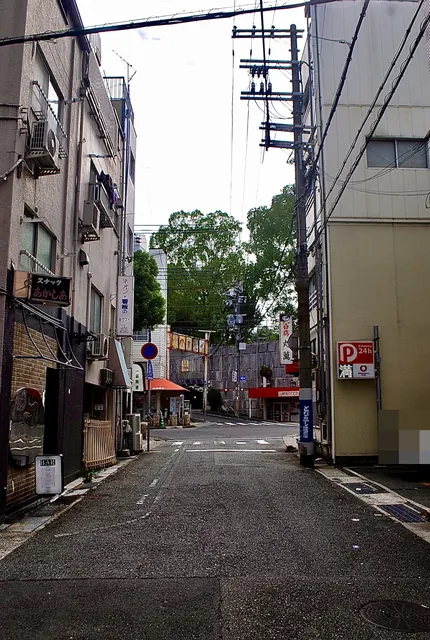 「スナック」の看板や「丸萬」の看板が並ぶ、坂の下へ続く道
