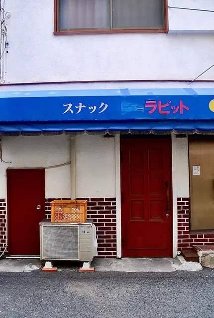 青い日よけと赤い扉、レンガ模様の壁の店