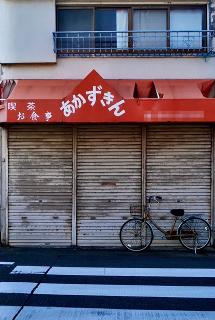 赤い日よけとシャッターのある店先に、自転車が止まっている