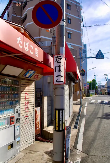 赤い日よけの角の店と、電柱に掛かる手書きの札