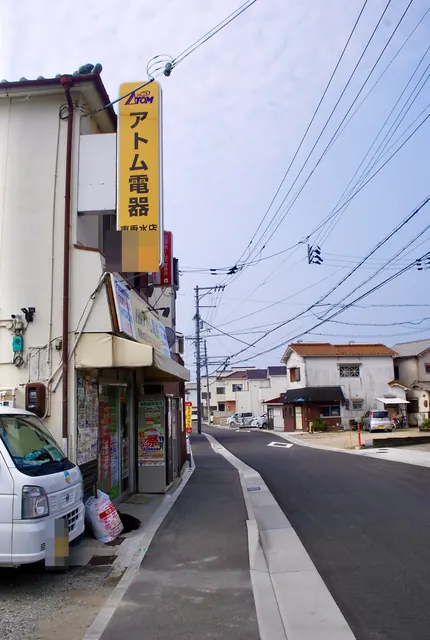 「アトム電器」の黄色い看板と、カーブして続く住宅街の道