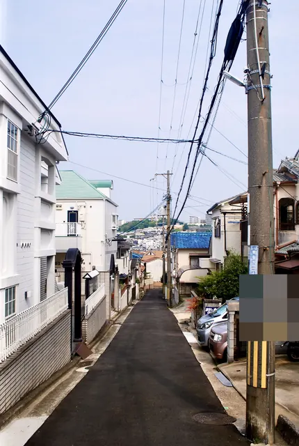 白い柵の家々のあいだから、遠くの街並みへ下る細い道