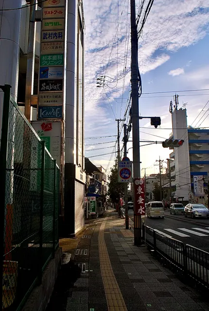看板の並ぶビルと、夕方の光に照らされた大通りの歩道