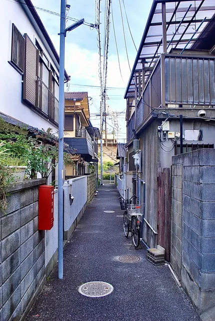 赤い消火器の箱と自転車のある、家々のあいだの細い路地
