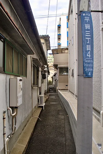 町名表示のある電柱と、家の壁に挟まれた細い路地