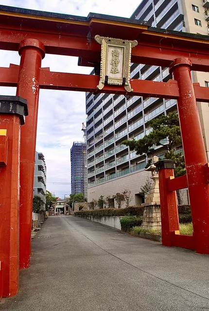 大きな朱色の鳥居を見上げ、奥に高層マンションが見える風景