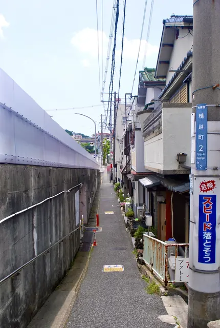 町名表示のある電柱と、高い壁と家々に挟まれた細い路地