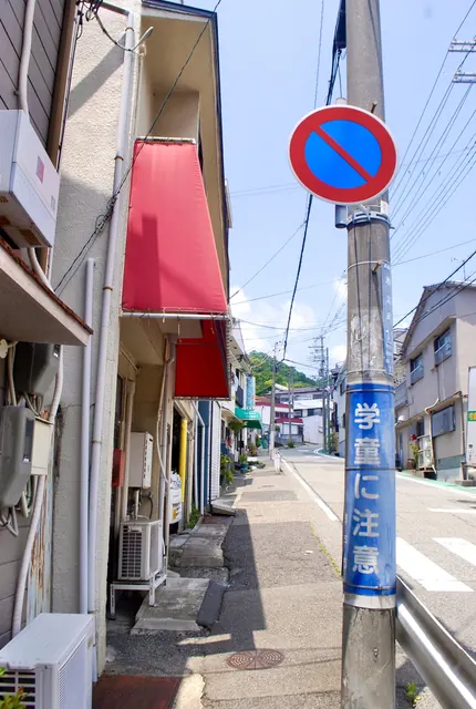 赤い日よけの家と、駐車禁止の標識が立つ緑の見える通り