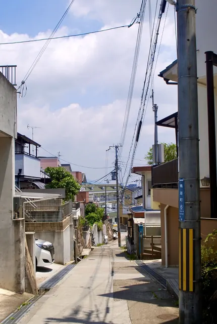 町名表示のある電柱の脇から、遠くの町並みへ下っていく坂道