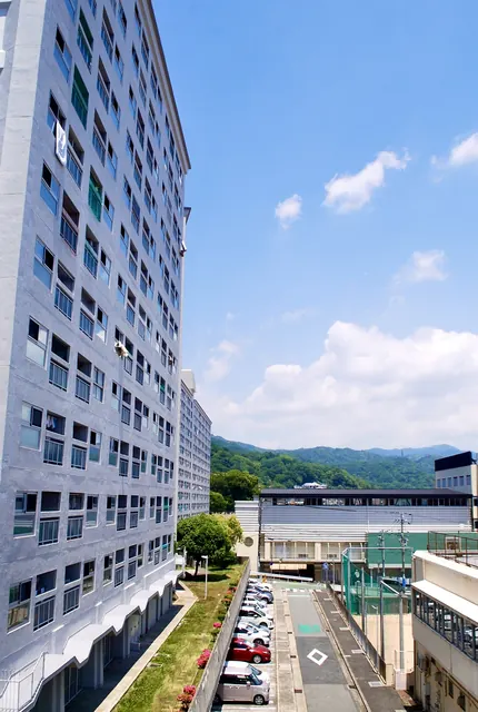 大きな団地の脇から、駐車場と緑の山並みを見渡す風景