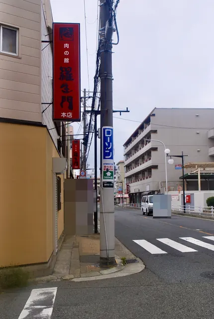 赤い縦看板とコンビニの案内が並ぶ、大通り沿いの角