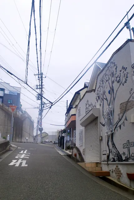 大きな木の絵が描かれた家の脇を、上へ続く坂道