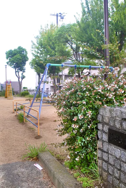 ピンクと白の花の咲く垣根と、ブランコのある公園