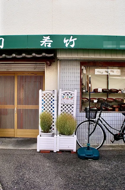 緑の日よけと格子戸、白い花台が並ぶ寿司屋の店先