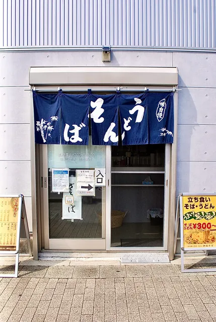 「そば うどん」の紺ののれんと、立て看板が並ぶ店の入口