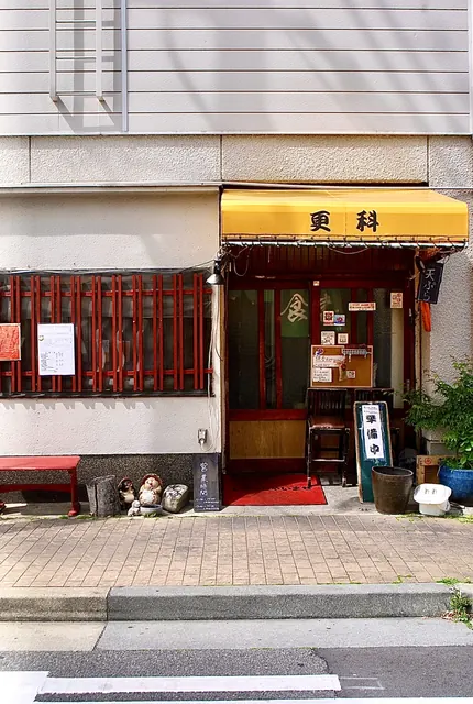 黄色い日よけと赤い格子、たぬきの置物が並ぶそば処の入口
