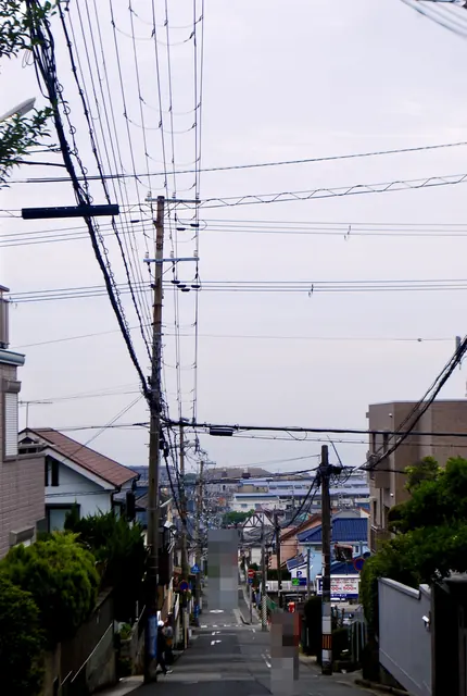 電柱と電線が続く坂の上から、遠くの家並みを見下ろす風景