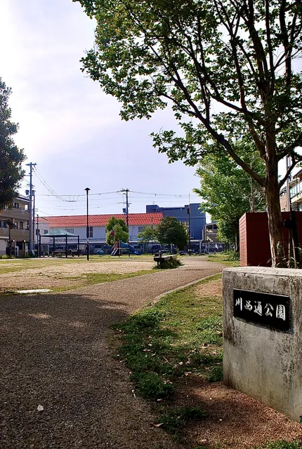 「川西通公園」の石の銘板と、広場の向こうの遊具