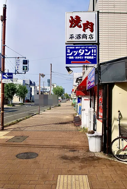 「焼肉 平沼商店」の看板と、並木の続く大通りの歩道