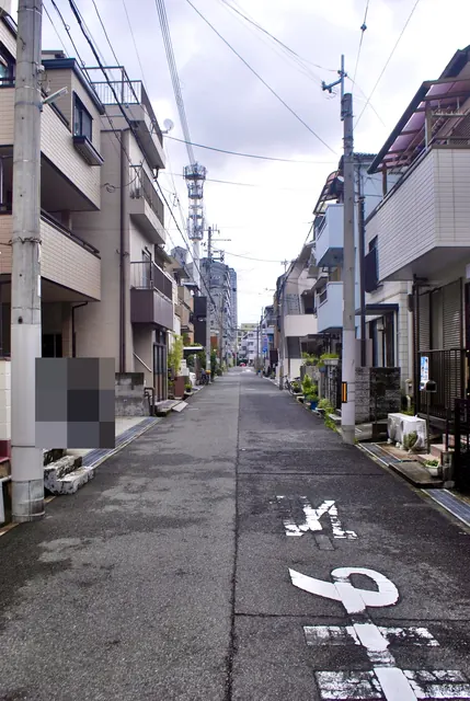 電柱と家々が並び、遠くのマンションまでまっすぐ続く住宅街の道