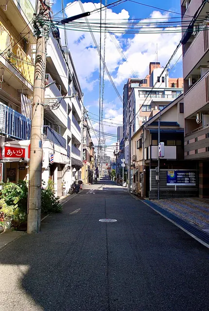 電柱が立ち、赤い日よけの店やサインポールが並ぶ、昼間の通り