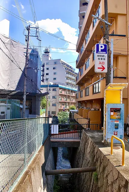 石積みの水路に小さな橋がかかり、電線と建物が見える風景