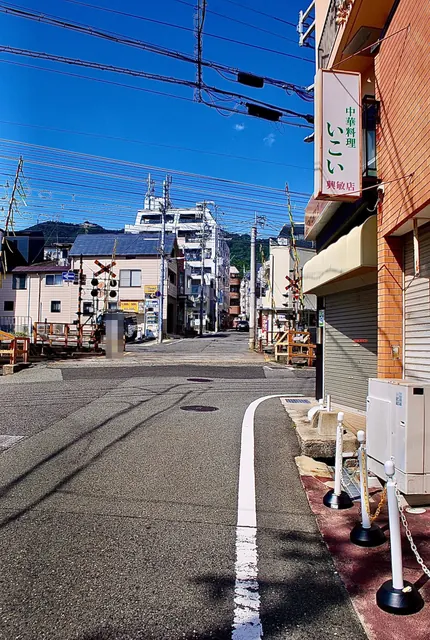 電線が幾重にも交差する青空の下、踏切の向こうに山が見える交差点