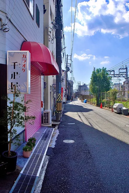 ピンク色のシャッターと日よけの店先に沿って、線路の見える道が続く風景