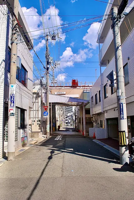 電柱の看板が並び、奥に商店街の入口が見える青空の下の通り