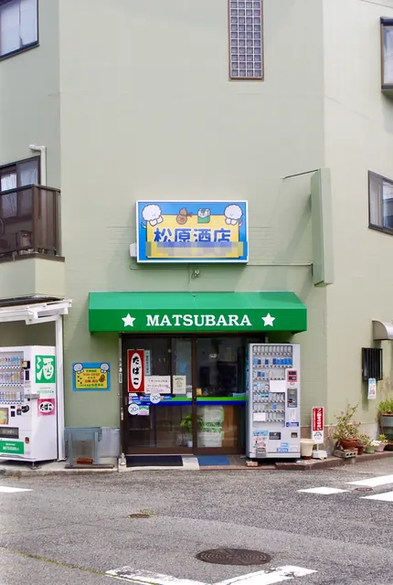 緑の日よけと自動販売機が並ぶ、角の酒店