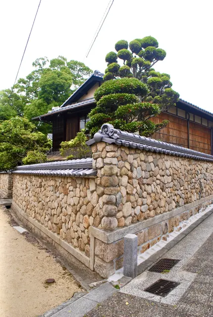 丸い石の石垣に瓦屋根をのせた塀と、手入れされた松の木