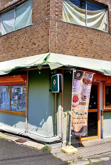 レンガの壁と緑のテントに、オーダーケーキののぼりが立つ店