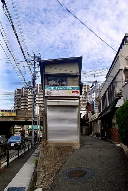 シャッターの小さな建物の脇から、看板の並ぶ路地へ続く風景