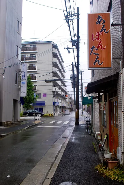 縦長の看板の立つ角から、交差点とマンションを見る風景
