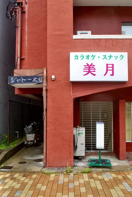 赤い壁の古いマンションの入口と、看板の残る軒