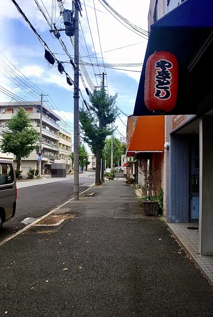 赤い「やきとり」の提灯の先に、並木の続く大通りの歩道